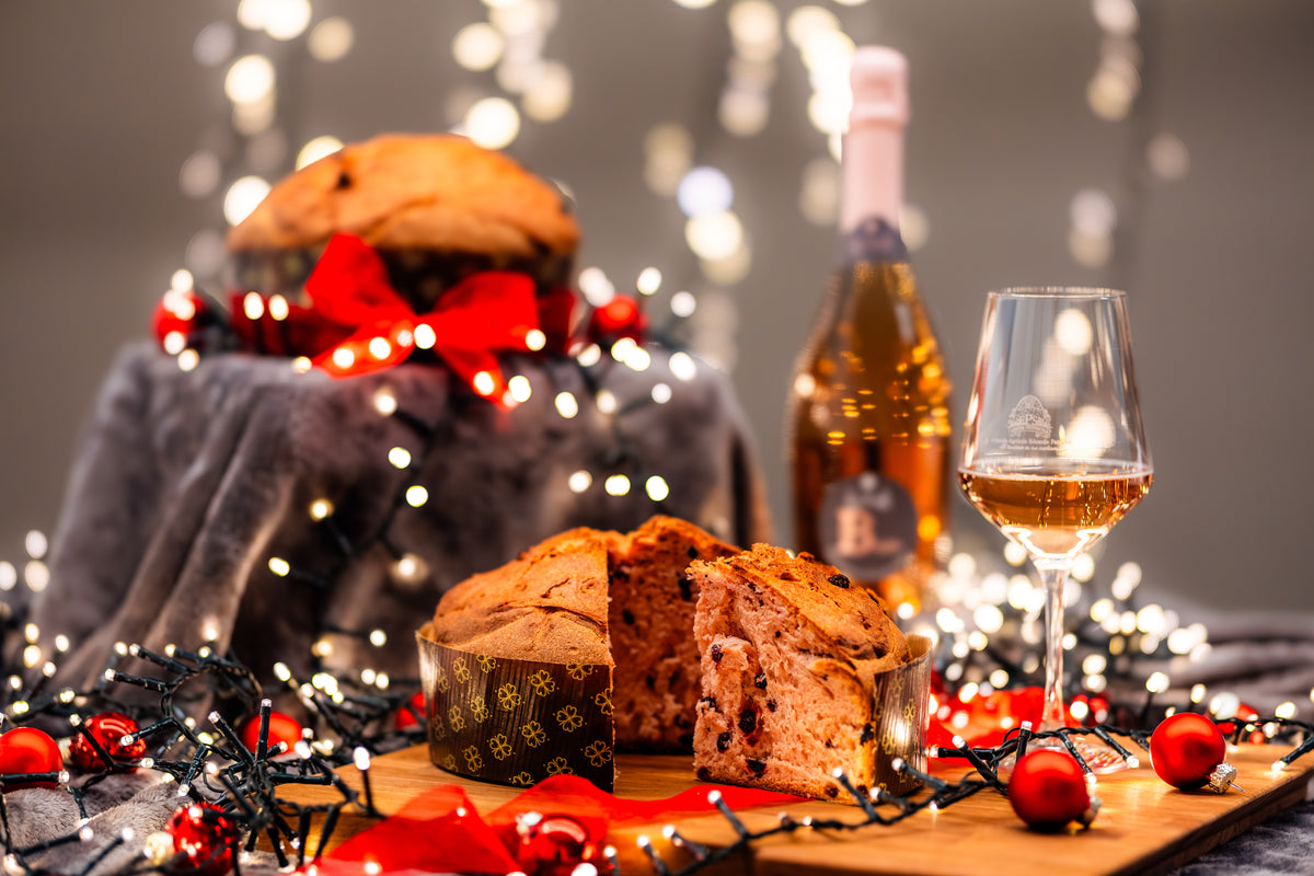 Разрезанный Panettone Rosa al Basin с бутылкой и бокалом вина среди рождественских огней и украшений.